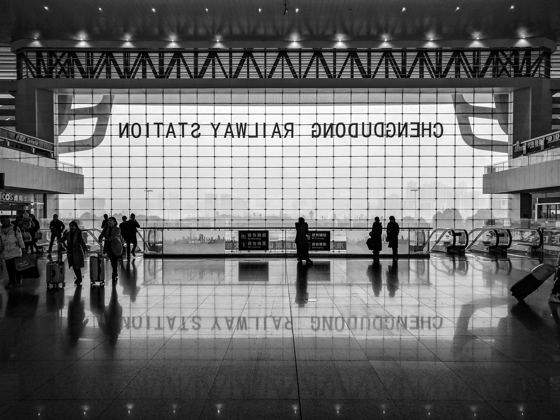 Black and white shot of station foyer with people and large window and reflection on floor